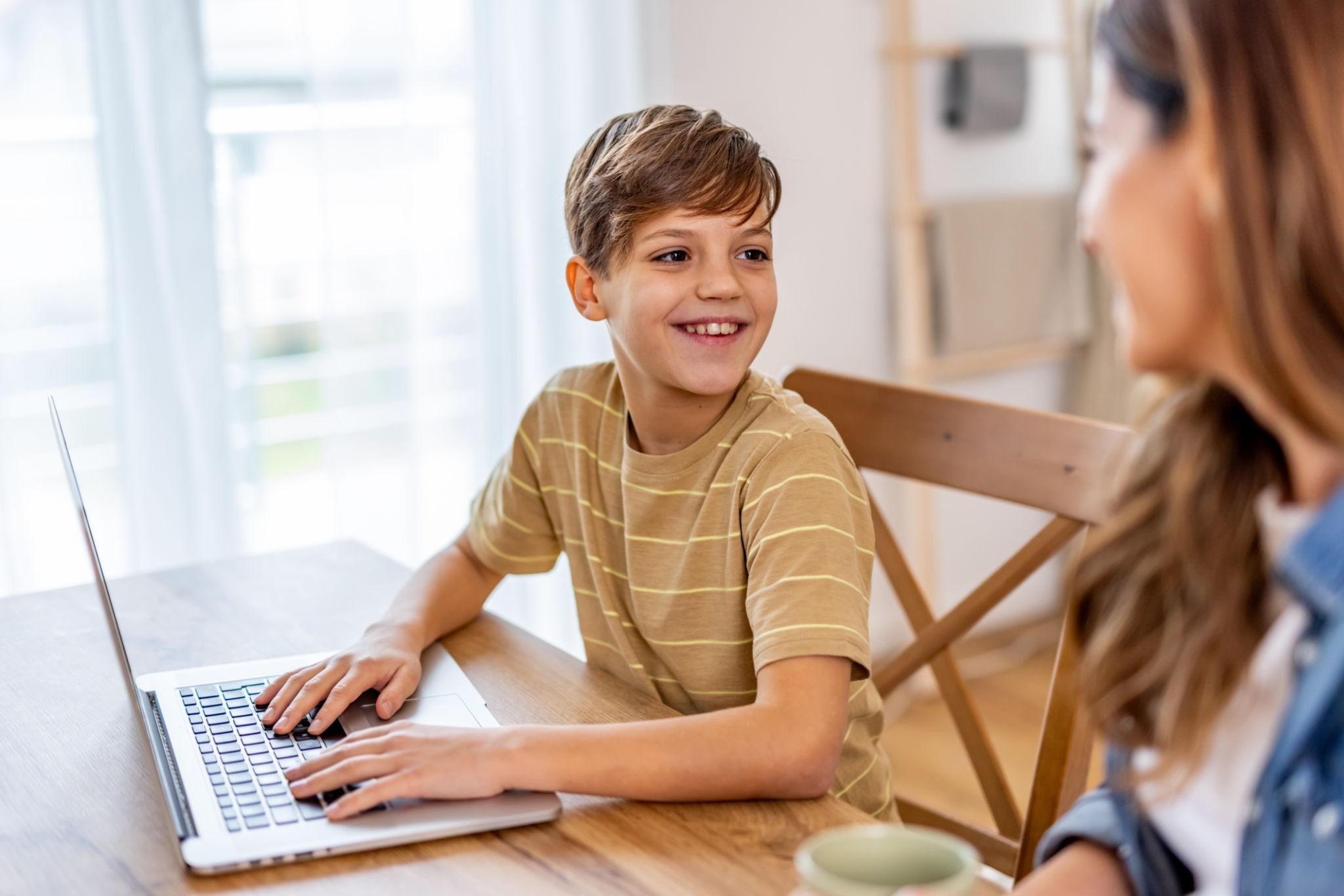 Boy smiling at a laptop during an online session with a parent beside him.